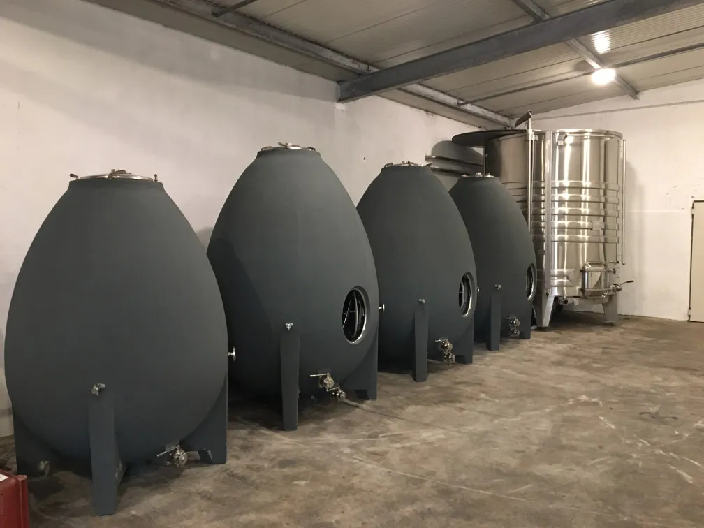 Quatre cuves en béton en forme d’œuf alignées dans la cuverie, une cuve inox au fond