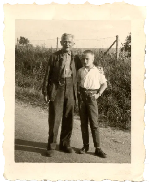 Photographie ancienne en noir et blanc : un homme âgé et un jeune garçon posent sur un chemin, devant les vignes
