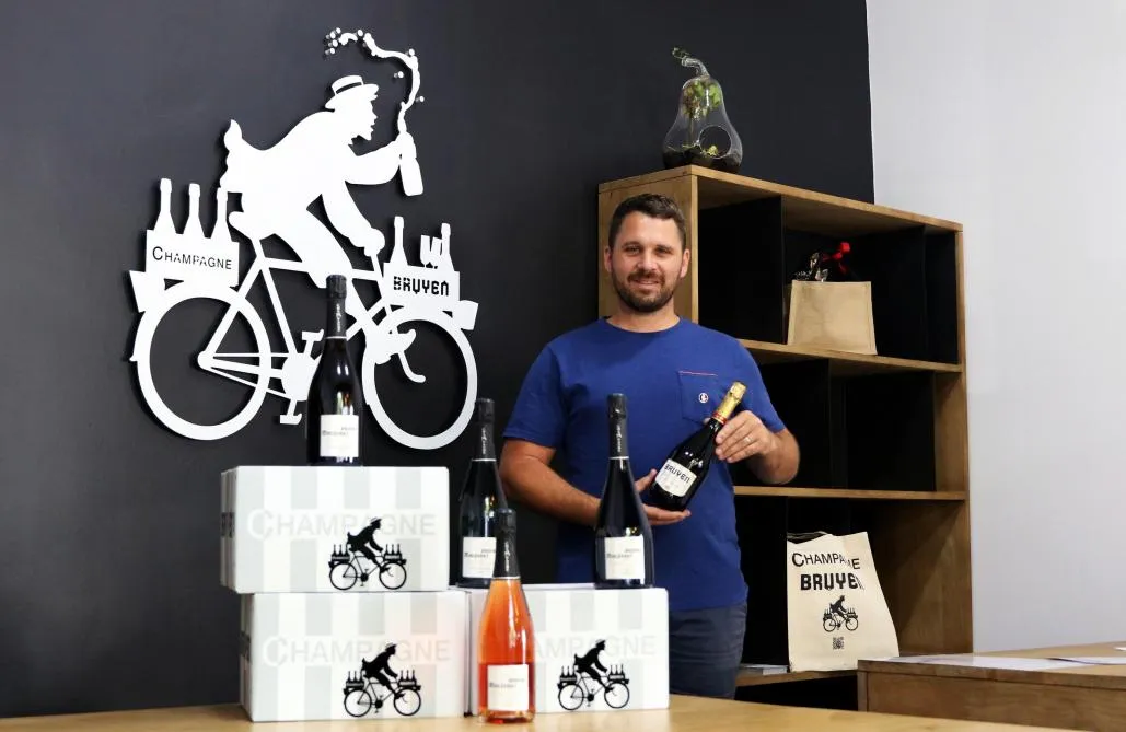Grégory Bruyen dans son bureau-boutique de la rue Libergier, une bouteille à la main, devant une grande silhouette blanche du livreur à vélo